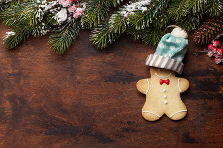 Christmas greeting card with gingerbread cookie and xmas fir tree branch over wooden backdrop. Top...