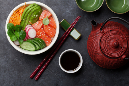 Poke bowl with salmon and vegetables, tea pot and cups. Traditional Hawaiian raw fish salad. Top viewの写真素材