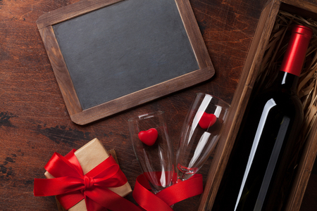 Valentine's day greeting card with red wine bottle and love gift box on wooden background. Top view with chalkboard for your greetings. Flat layの写真素材