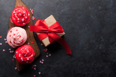 Valentine's day greeting card with delicious sweet cupcakes and gift box on stone background. Top view with space for your greetingsの写真素材