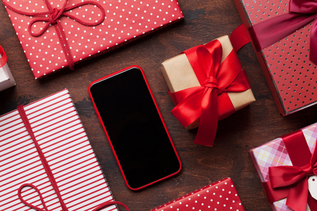 Valentine's day greeting card with gift boxes and smartphone on wooden background. Top view with space for your greetings or smart phone app. Flat layの写真素材