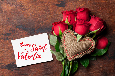 Valentine's day greeting card with red rose flowers bouquet and knitted heart on wooden background. Bonne Saint Valentin France. Top view with space for your greetingsの写真素材