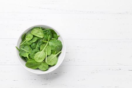 Fresh garden spinach salad bowl on wooden table. Top view with copy spaceの写真素材
