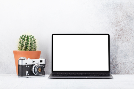 Loft home office workplace with blank white screen laptop computer, plant and camera. With copy space for your mockup or textの写真素材
