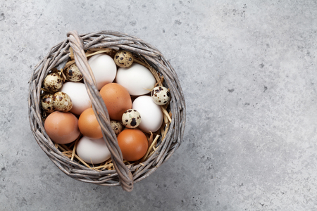 Hen and quail eggs in basket on stone table. Easter greeting card. Top view with space for your greetingsの写真素材