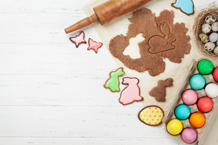 Easter greeting card with cooking gingerbread cookies and colorful eggs. Top view on wooden table...