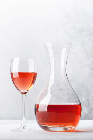Rose wine in glass and decanter on wooden table. In front of stone wall with space for your textの写真素材