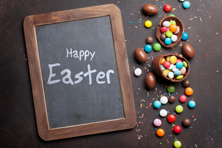 Easter greeting card with chocolate eggs and colorful candies. Top view with chalkboard for your greetingsの写真素材