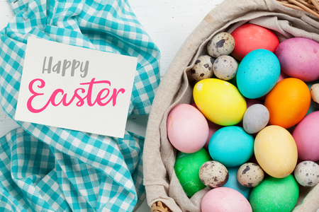 Easter greeting card with colorful easter eggs in basket. Top view on wooden table with space for your greetingsの写真素材