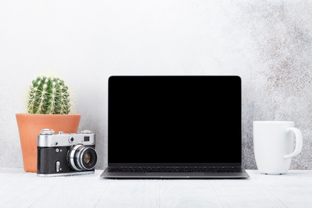 Loft home office workplace with blank black screen laptop computer, camera and cactus. With copy space for your mockup or textの写真素材