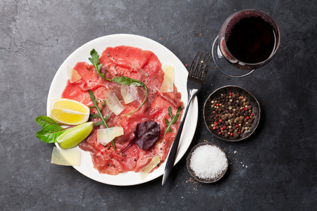 Marbled beef carpaccio with arugula, lemon, parmesan cheese with red wine glass. Top viewの写真素材