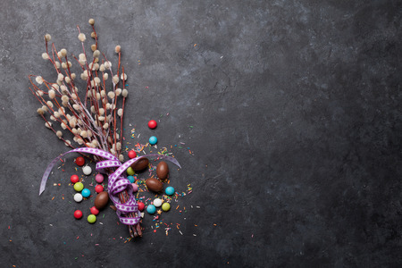 Easter greeting card with chocolate eggs and colorful candies. Top view on stone table with space...