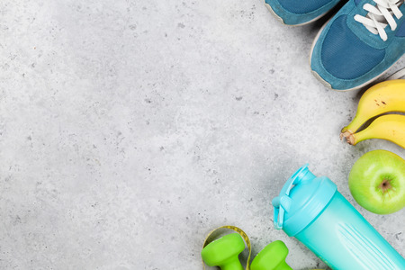 Fitness and healthy food concept. Sneakers, fruits and drink bottle on stone table. Top view with copy space for your textの写真素材
