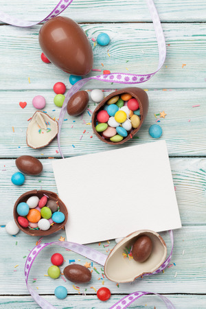 Easter greeting card with chocolate eggs and colorful candies. Top view on wooden table with space for your greetingsの写真素材