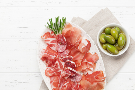 Traditional spanish jamon, prosciutto crudo, italian salami, parma ham. Antipasto plate and olives. Top view flat lay. With copy space