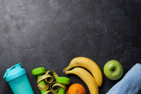 Fitness and healthy food concept. Dumbbells, apple and drink bottle on stone table. Top view with copy space for your textの写真素材