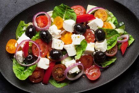 Greek salad with cucumber, tomato, pepper, lettuce, onion, feta cheese and olives, dressed with olive oil. Top view closeupの写真素材
