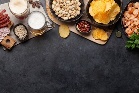 Draft beer and snacks on stone background. Nuts, chips, sausages and shrimps. Flat lay. Top view with copy spaceの写真素材