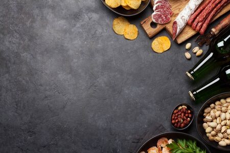 Draft beer and snacks on stone background. Nuts, chips, sausages and shrimps. Flat lay. Top view with copy spaceの写真素材