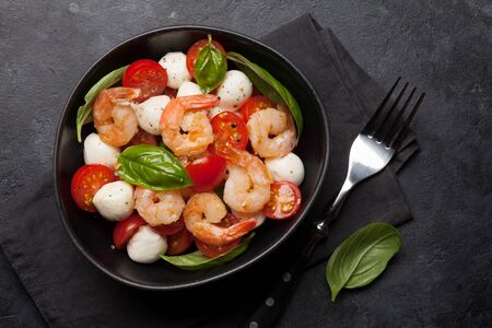 Fresh caprese salad with cherry tomatoes, mozzarella, basil leaves and grilled shrimps. Flat lay. Top viewの写真素材