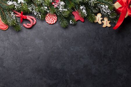Christmas card with gingerbread cookies and fir tree branch covered by snow on stone background. Top...