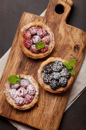 Set of sweet cakes with berries on wooden board. Strawberry, raspberry and blackberryの写真素材
