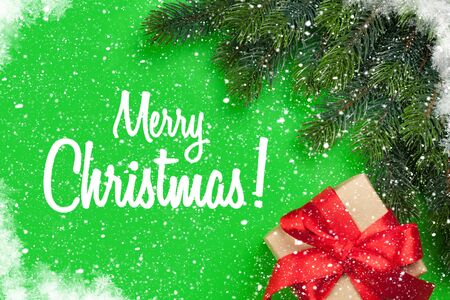 Christmas greeting card with gift box and fir tree branch over green background. Xmas backdrop. Top view with greetingsの写真素材