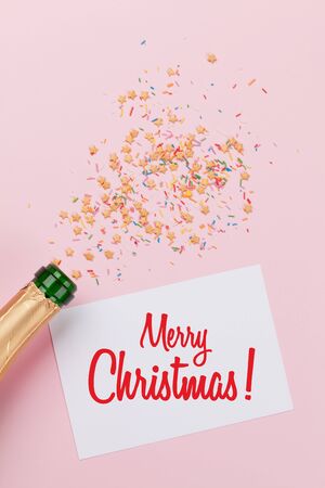 Christmas greeting card, champagne and star shaped sweets over pink background. Top view. Flat layの写真素材