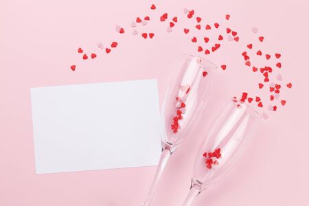 Champagne glasses, greeting card and heart shaped sweets holiday template. Christmas, Birthday or Valentines'day over pink background. Top view with space for your greetings. Flat layの写真素材