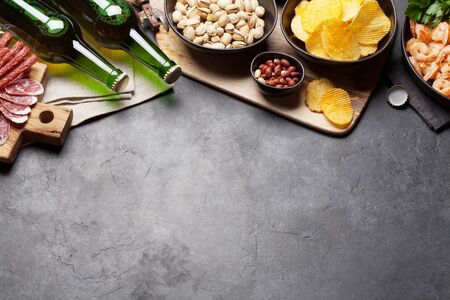Draft beer and snacks on stone background. Nuts, chips, sausages and shrimps. Top view with copy spaceの写真素材