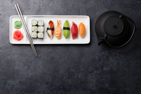Japanese sushi set. Sashimi, maki rolls and green tea. On plate over stone background with space for your text. Top view flat layの写真素材