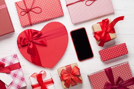 Valentine's day greeting card with gift boxes and smartphone on wooden background. Top view with space for your greetings or smart phone app. Flat layの写真素材