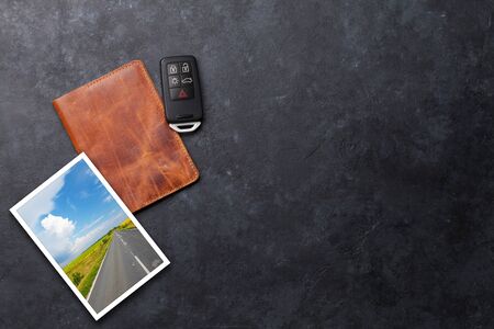 Travel vacation concept with passport, trip photo and car key on stone backdrop. Top view with copy...