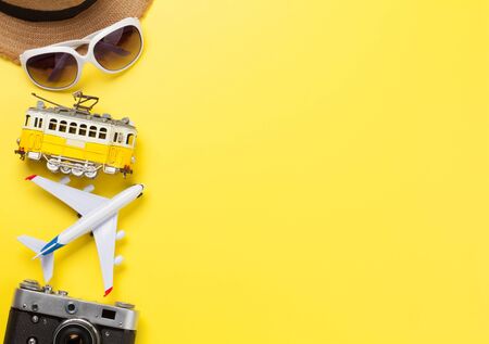 Travel concept with camera, sun hat, sunglasses, tram and airplane toy over yellow sunny backdrop. Top view flat lay with copy spaceの写真素材