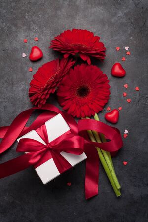 Valentines day greeting card with gerbera flower bouquet and gift box over stone background. Top view flat layの写真素材