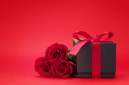 Valentines day greeting card with rose flower bouquet and gift box over red background with copy space for your greetingsの写真素材