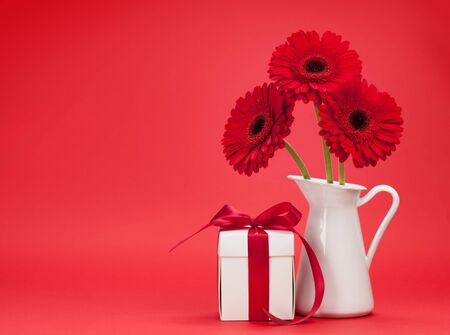 Valentines day greeting card with gerbera flower bouquet and gift box in front of red background with space for your greetingsの写真素材