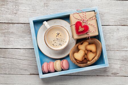 Valentines day greeting box with coffee cup, macaroons and gingerbread cookies over wooden background. Top view flat lay