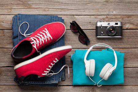 Clothing and accessories. Sneakers, jeans, camera and headphones. Urban outfit for everyday or travel vacation on wooden background. Top view flat layの写真素材