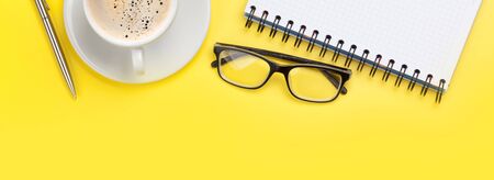 Office yellow workplace backdrop with coffee cup and supplies. Wide flat lay. Top view with copy...