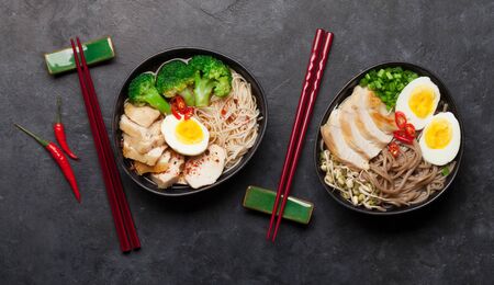 Asian noodle ramen soups with chicken, vegetables and eggs on stone background. Top view flat lay