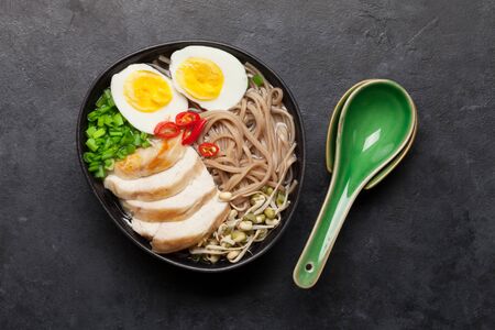 Asian noodle ramen soup with chicken, vegetables and eggs on stone background. Top view flat lay
