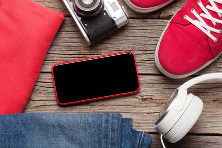 Clothing and accessories. Sneakers, jeans, headphones and smartphone. Urban outfit for everyday or travel vacation on wooden background with copy space on phone screen. Top view flat layの写真素材