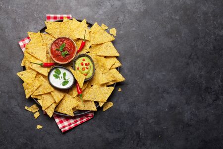 Mexican nachos chips with various sauces - guacamole, salsa and sour cream. Top view flat lay on stone table with copy spaceの写真素材