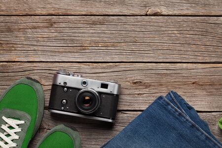 Clothing and accessories. Sneakers, jeans and camera. Urban outfit for everyday or travel vacation on wooden background with copy space. Top view flat layの写真素材