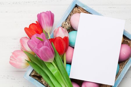 Easter greeting card with easter eggs and tulip flowers over wooden background. Top view flat lay...
