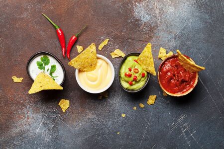 Mexican nachos chips with various sauces - guacamole, salsa, cheese and sour cream. Top view flat lay on stone table with copy spaceの写真素材