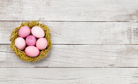 Easter greeting card with colorful easter eggs in nest on wooden background. Top view flat lay with space for your greetingsの写真素材