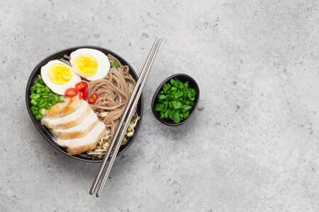 Asian noodle ramen soup with chicken, vegetables and eggs on stone