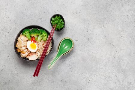 Asian noodle ramen soup with chicken, vegetables and eggs on stone background. Top view flat lay...
